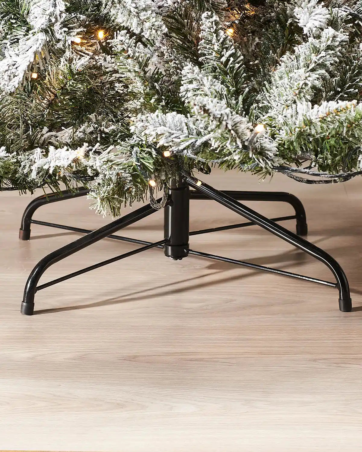 Close-up of the black metal stand and lower snow flocked branches of a 5 ft pre-lit Christmas tree