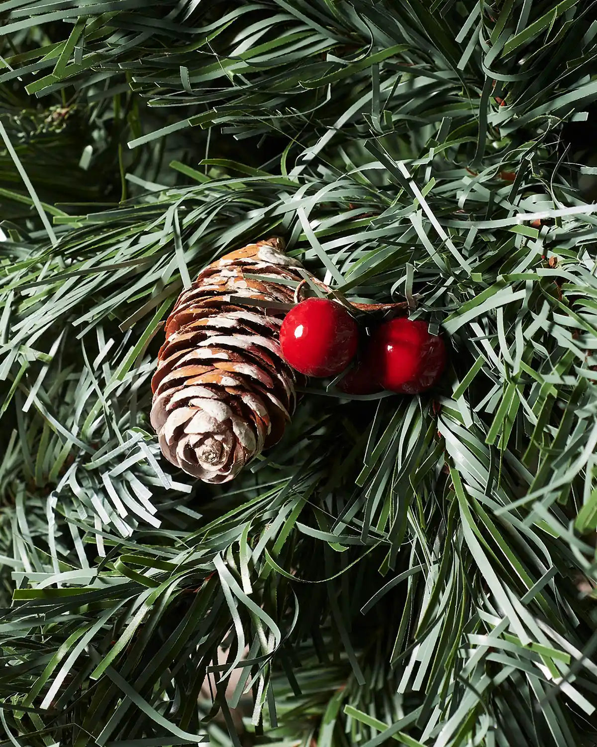Close-up of a frosted pinecone and red berries on a Scandinavian blue spruce Christmas tree