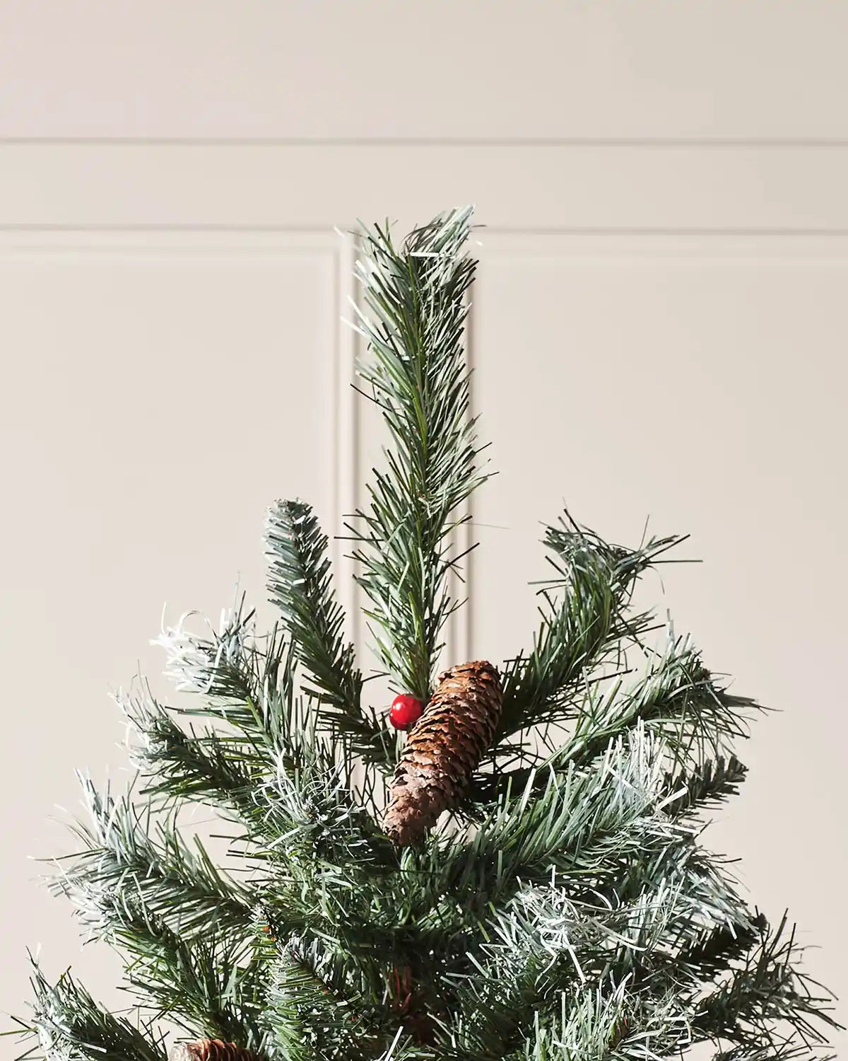 Top section of a Scandinavian blue spruce Christmas tree with frosted tips, pinecone and red berry detail
