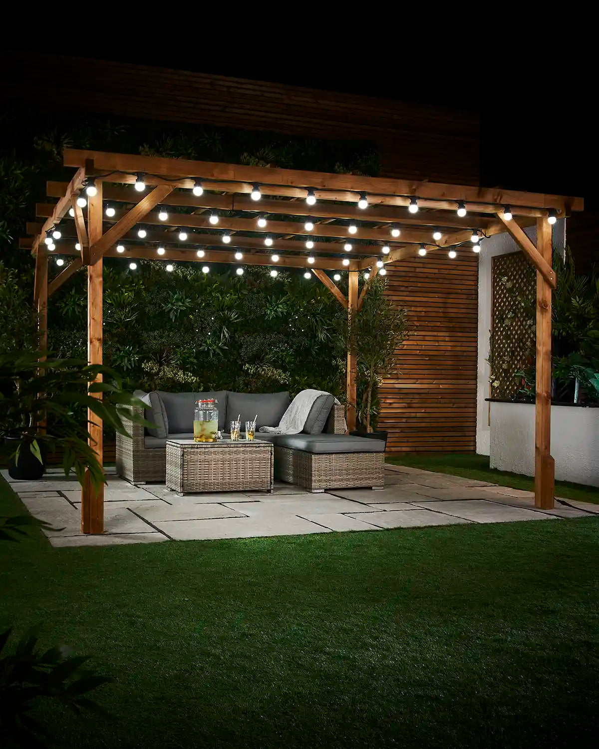 White festoon bulbs displayed across a wooden pergola above an outdoor seating area.