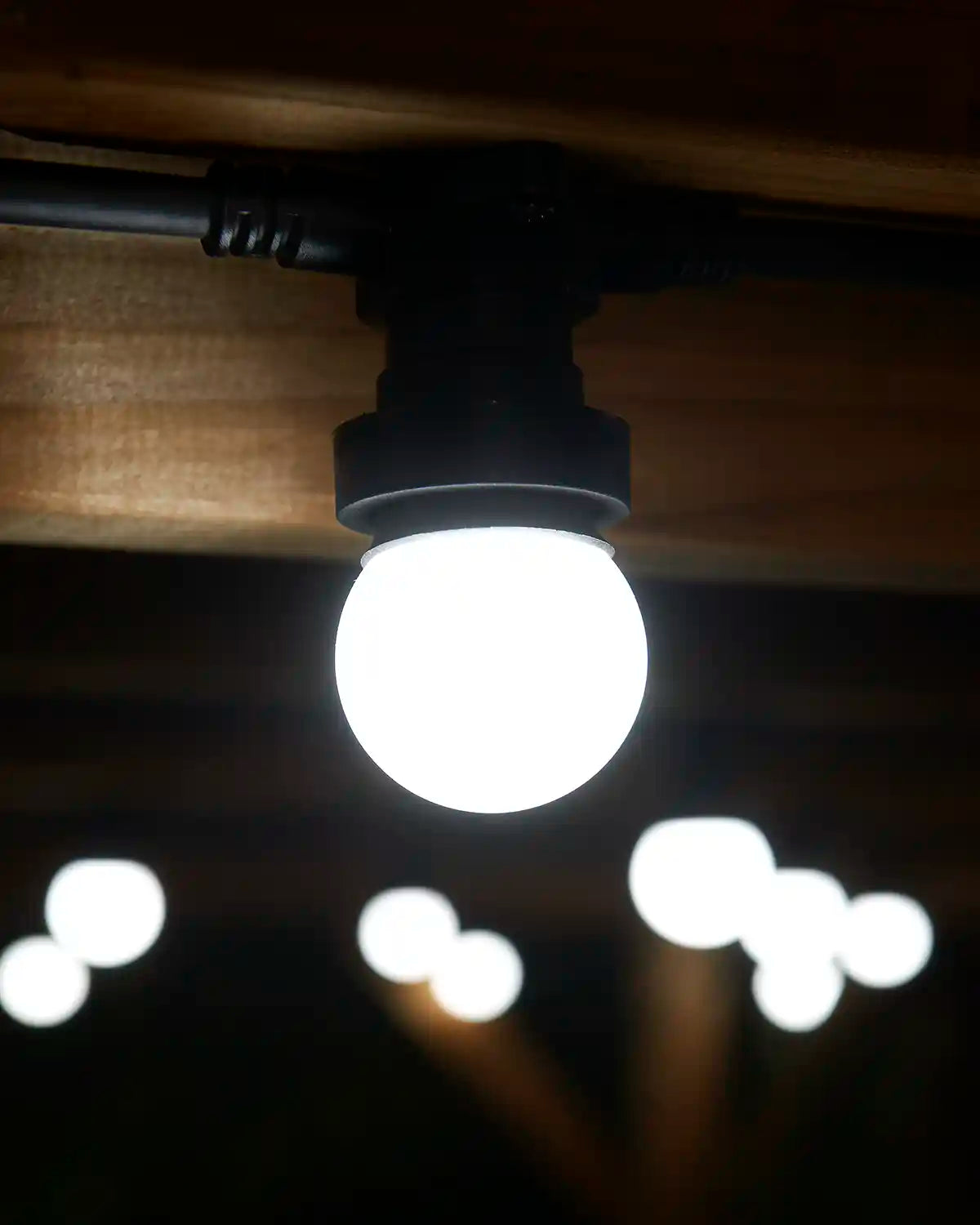 White festoon bulb fitted to a black E27 socket beneath a wooden pergola.