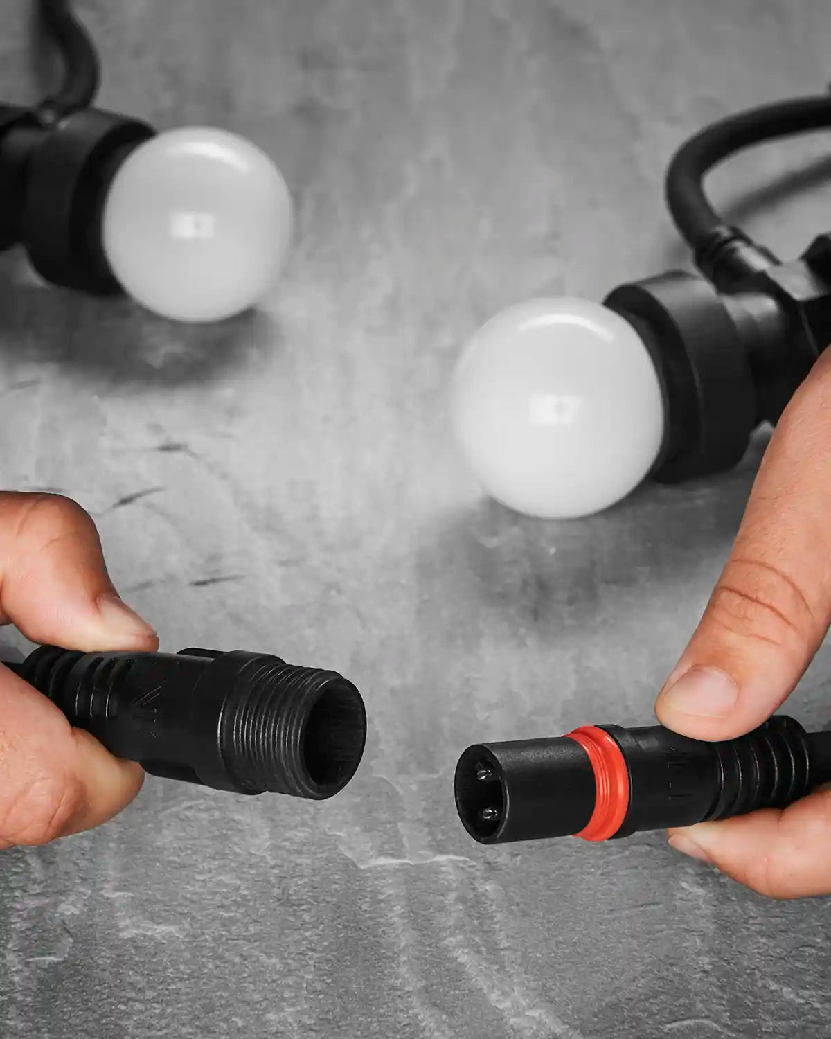 Hands connecting a Festoon Series cable with white bulbs shown in the background.