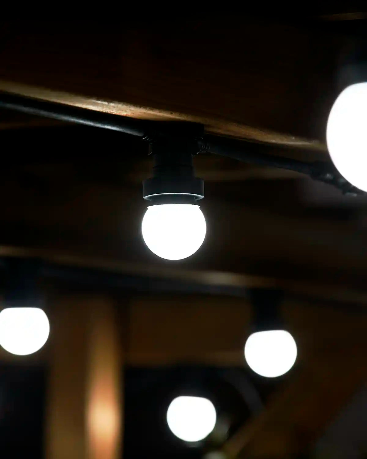White festoon bulb hanging from a black socket with blurred bulbs in the background.