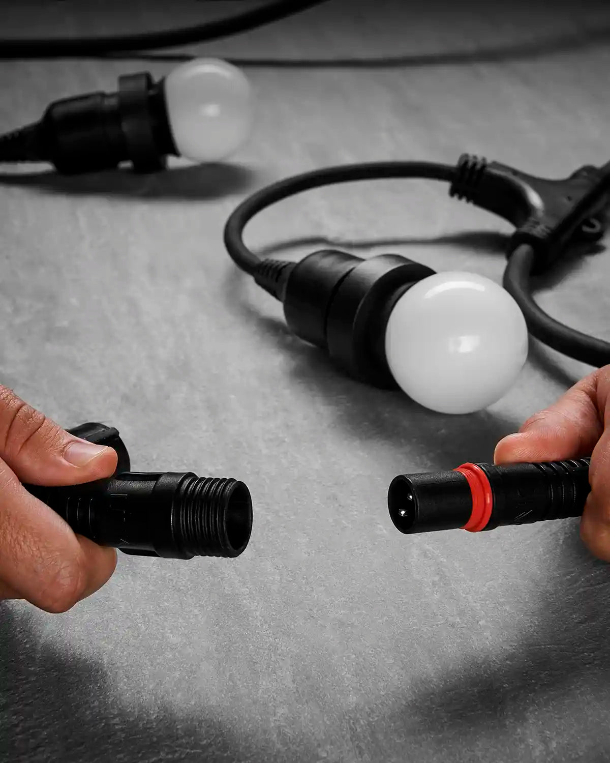 Hands connecting the waterproof plug ends of a black Festoon Series long drop belt.