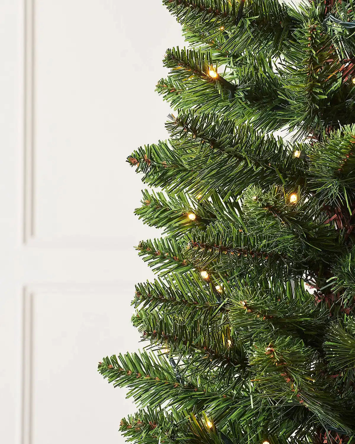 Close-up of green pencil Christmas tree branches with warm white LED lights