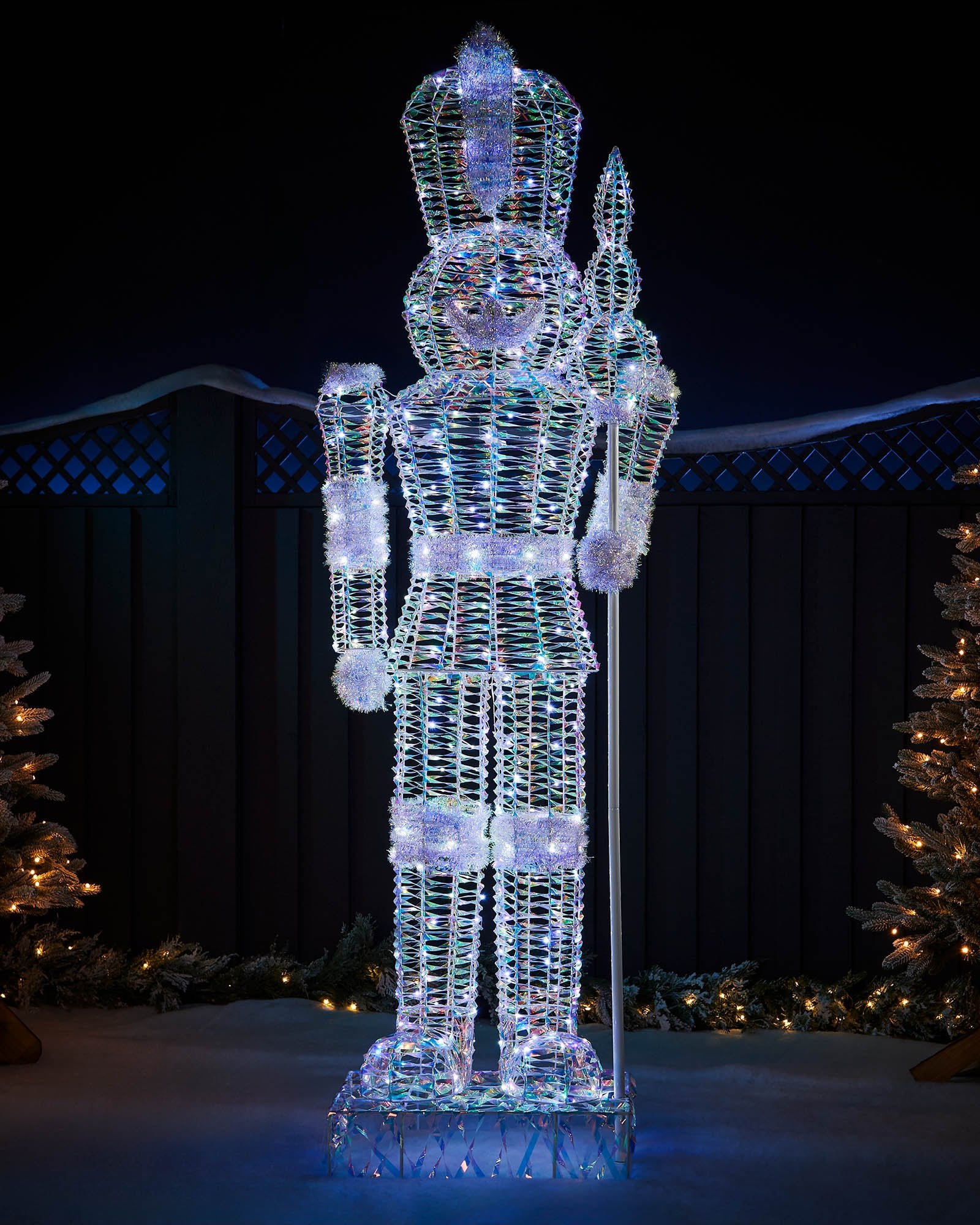 6.5ft pre-lit iridescent Nutcracker with white LEDs, staff and tinsel details in an outdoor display.