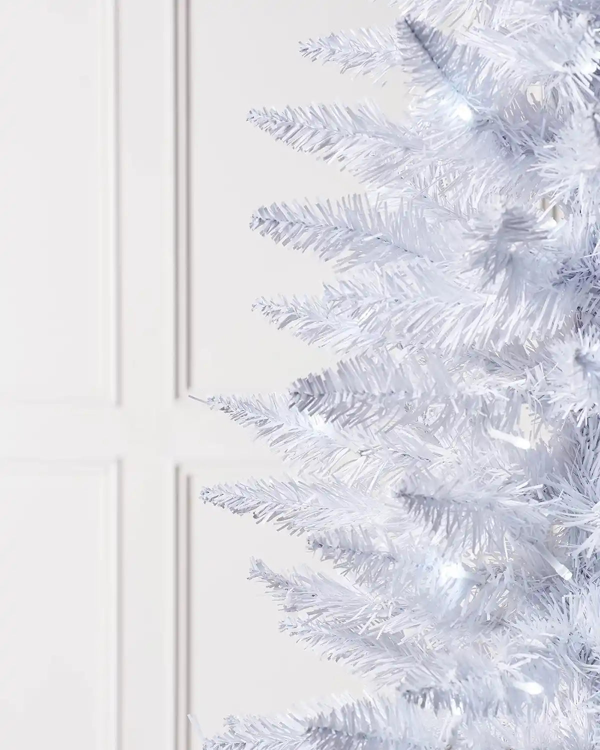 Close-up of white pencil Christmas tree branches with white LED lights