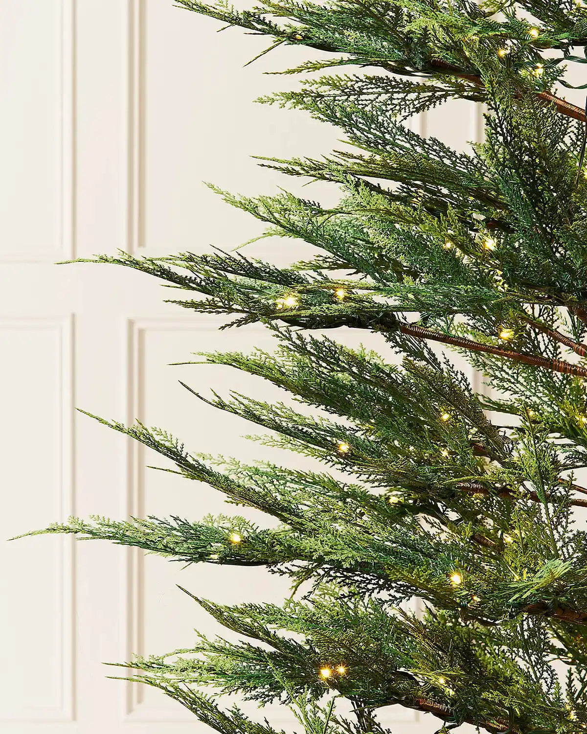 Close-up of 6.5ft cypress fir Christmas tree branches with warm white light setting in front of white panelling