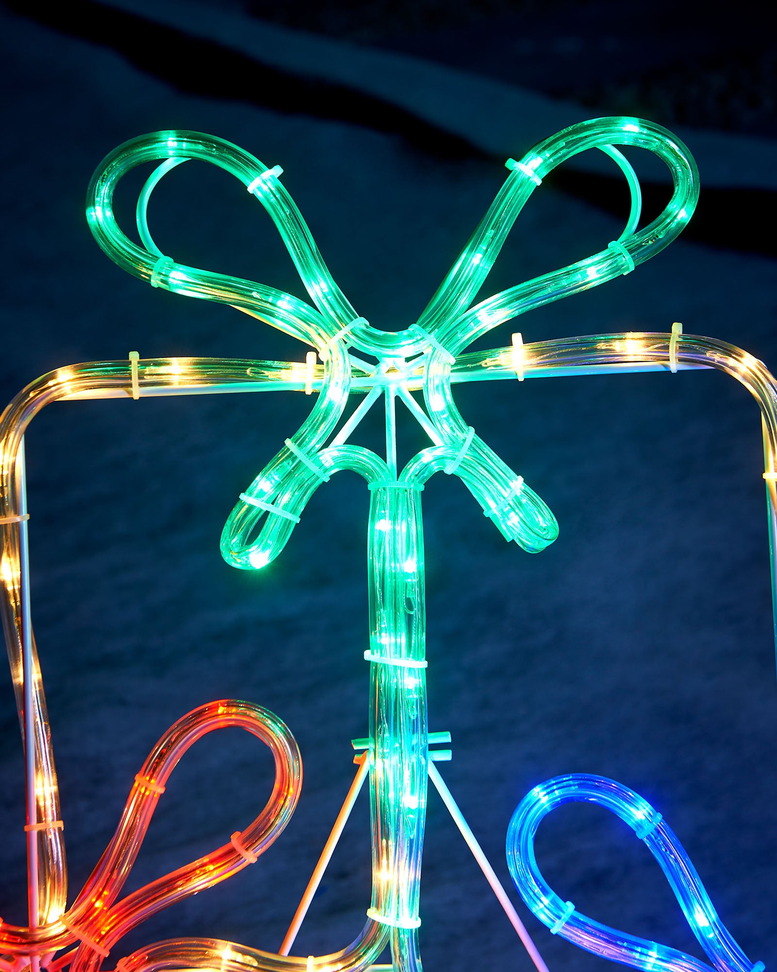 Detail of the green, red and blue illuminated bows on the gift box rope light display
