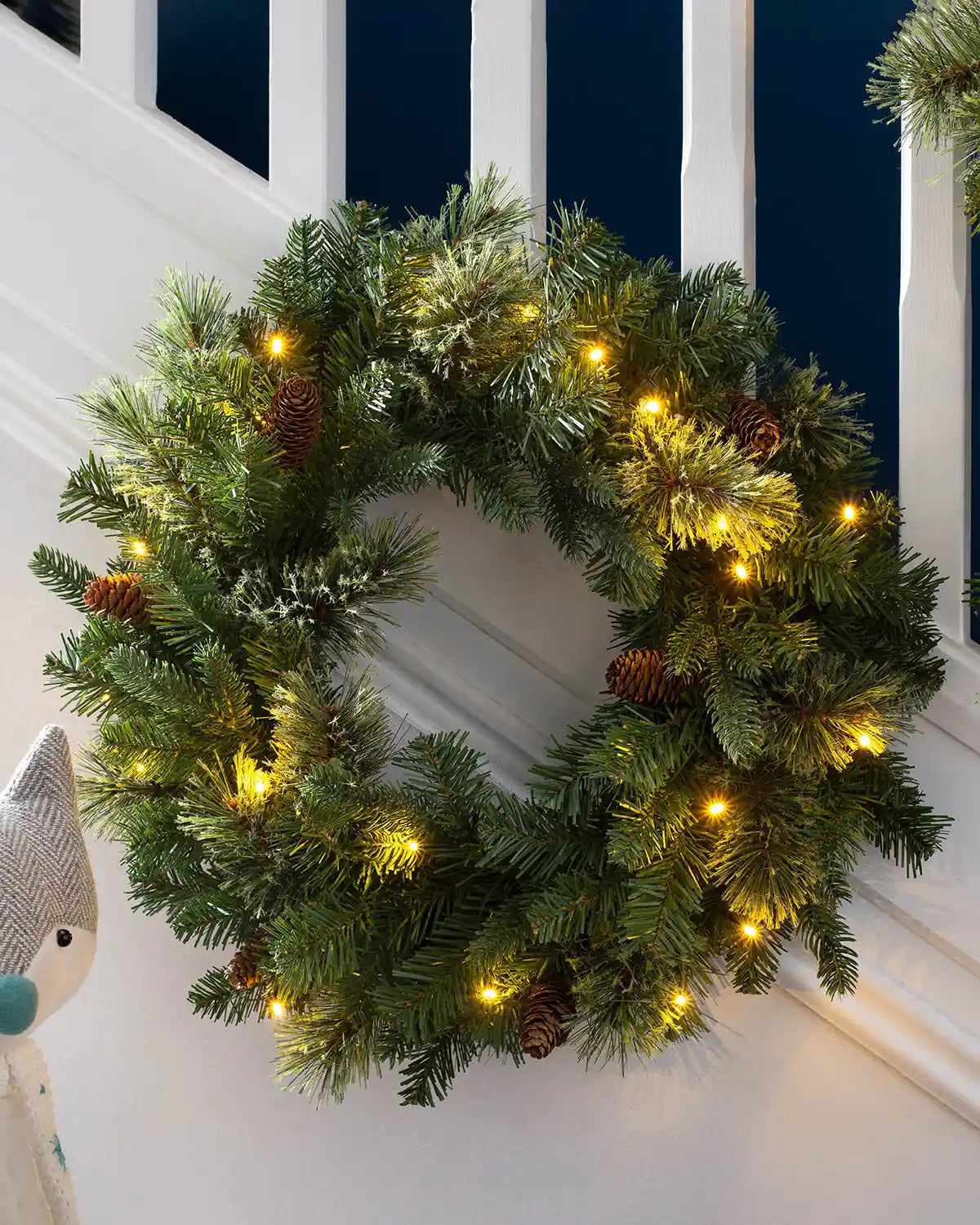 Pre-lit natural pine Christmas wreath styled by a staircase with pinecones and warm white lights