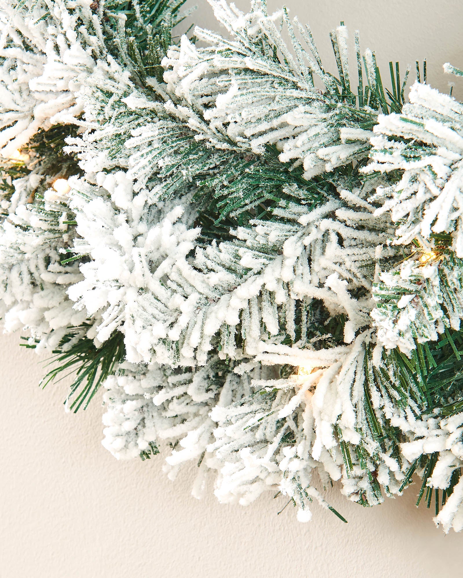 Close-up of dense green spruce-style wreath tips covered with artificial snow and warm white lights