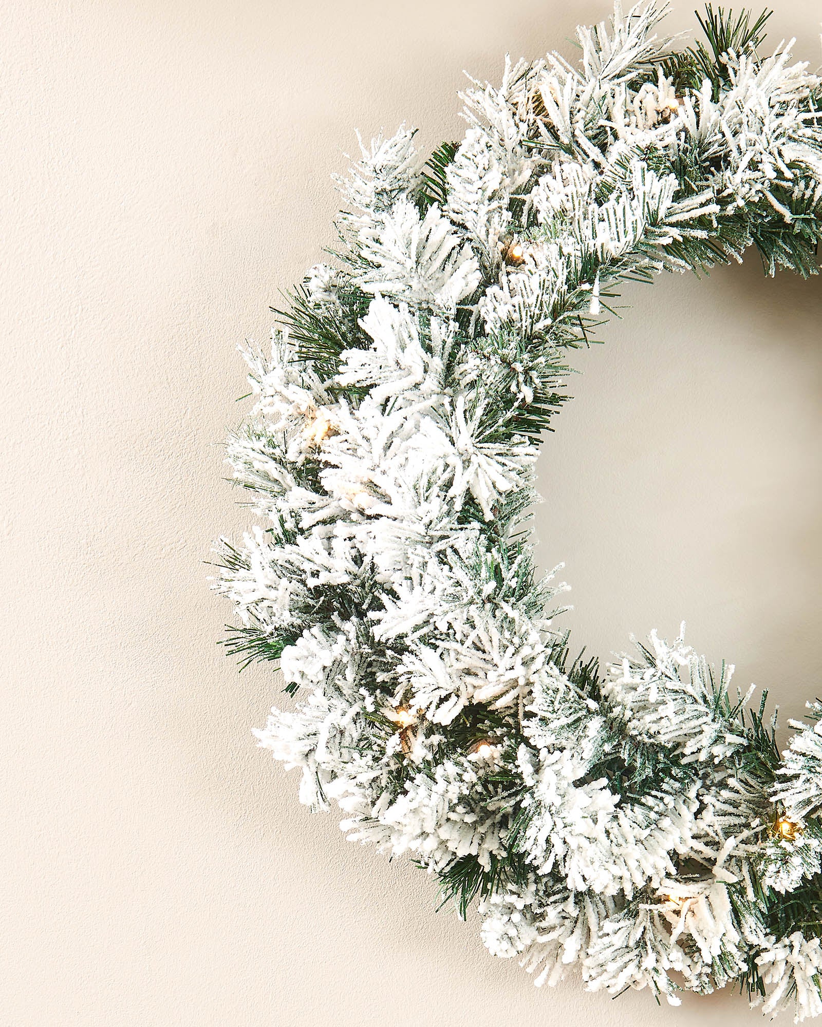 Close-up of a 60cm snow-flocked spruce wreath with warm white LEDs on a neutral wall