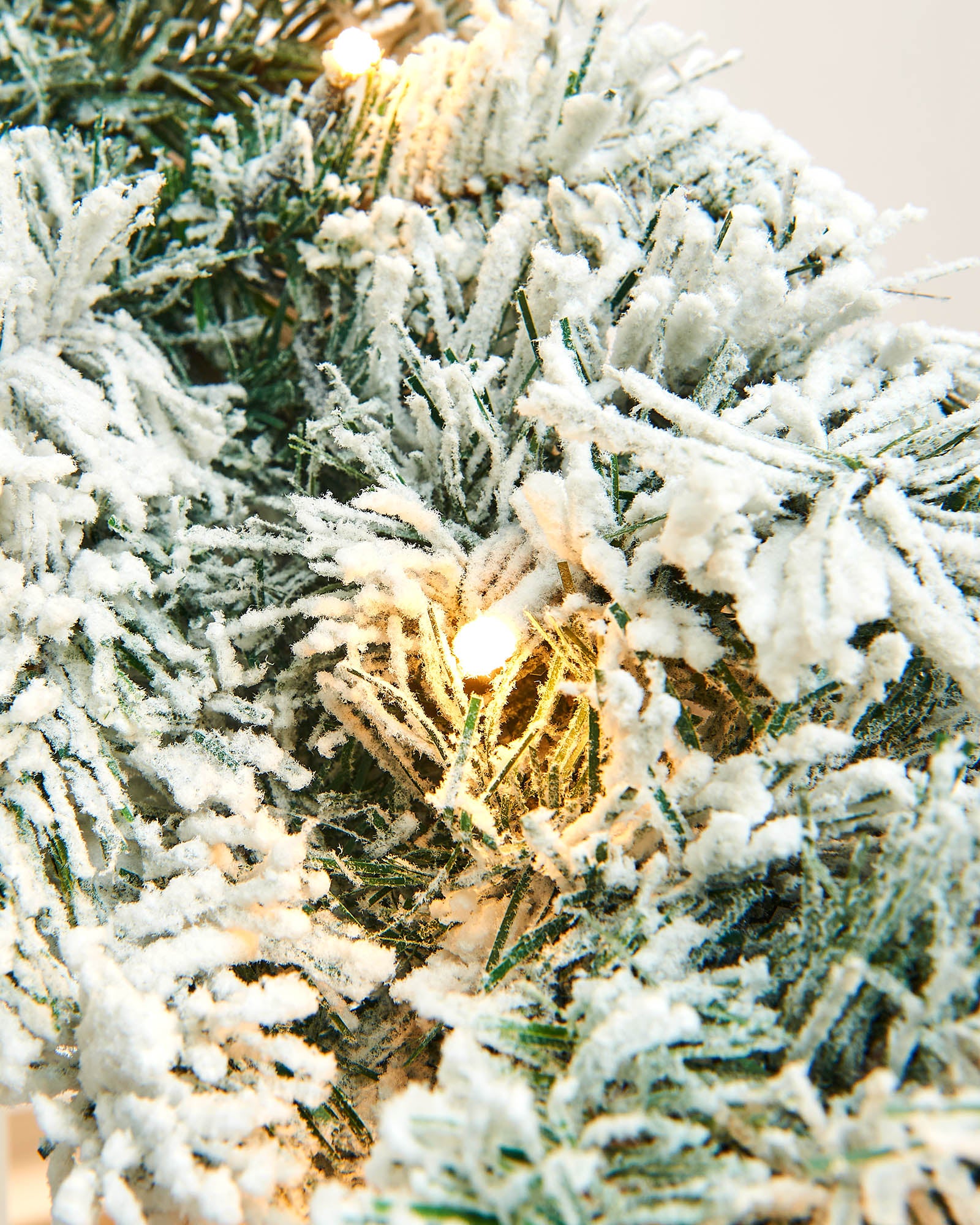 Close-up of a warm white LED glowing among snow-flocked spruce wreath branches