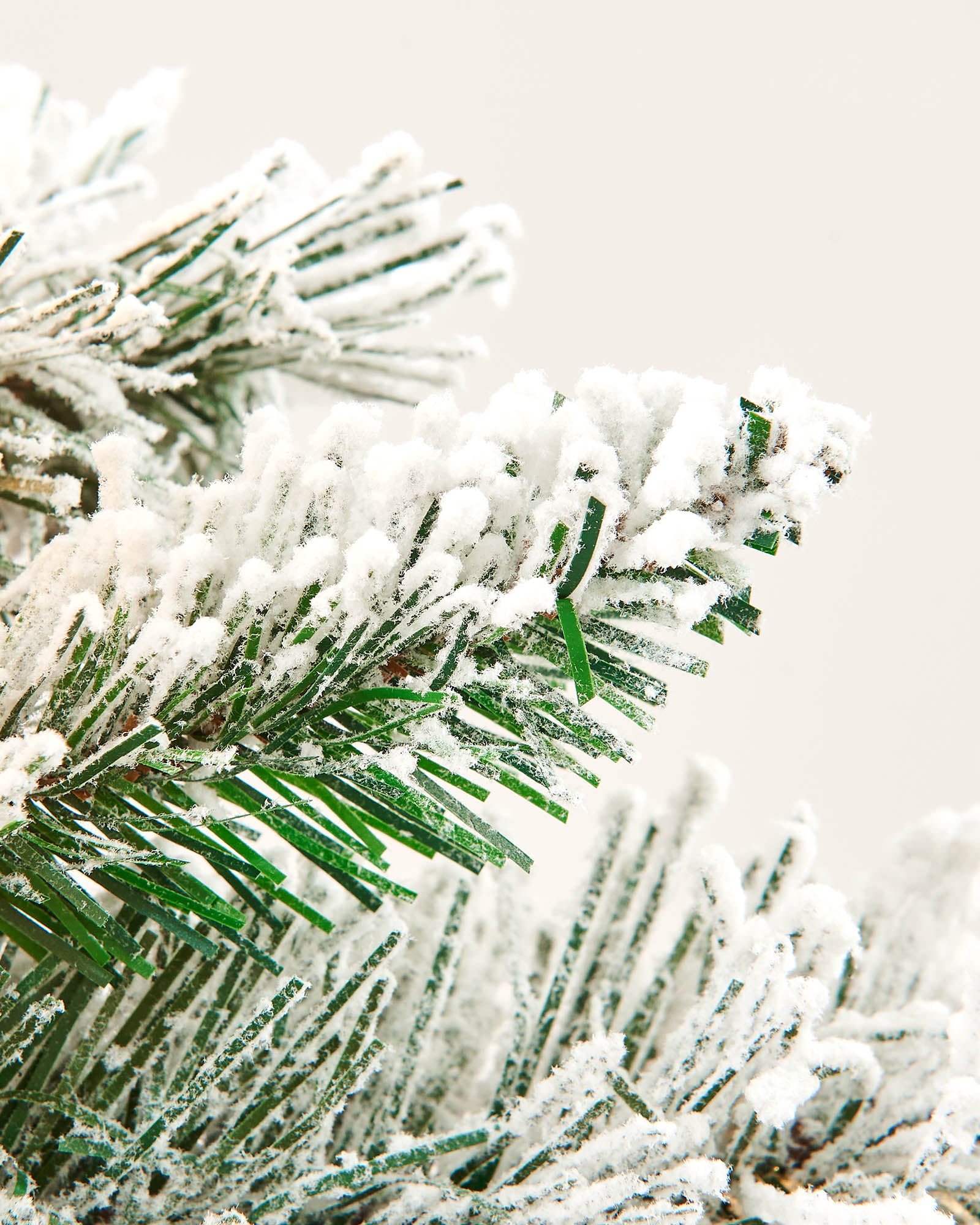 Close-up of green PVC wreath branches with a heavy snow-flocked finish