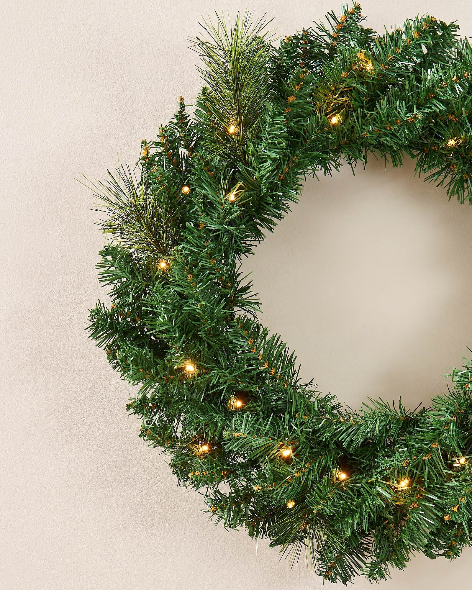 Close-up of a green Christmas wreath with mixed foliage and warm white LED lights