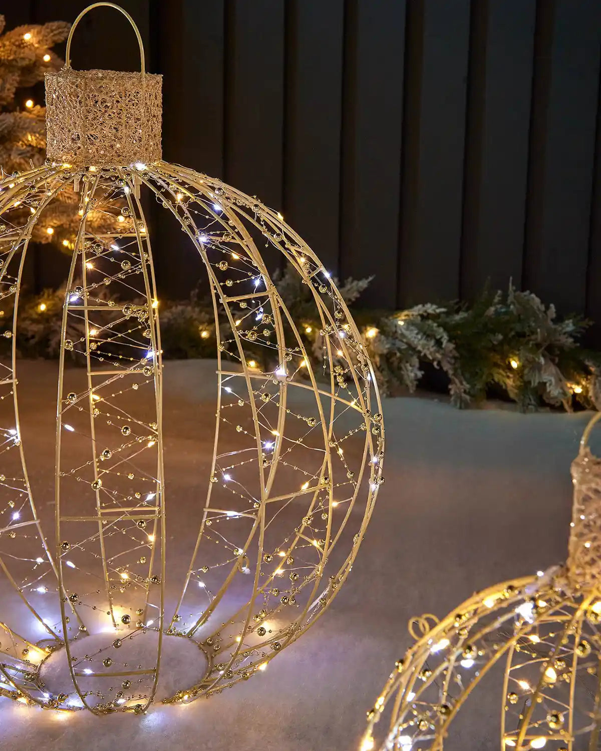 Close-up of a large gold bauble silhouette with metal frame, beaded strands and mixed white lights.