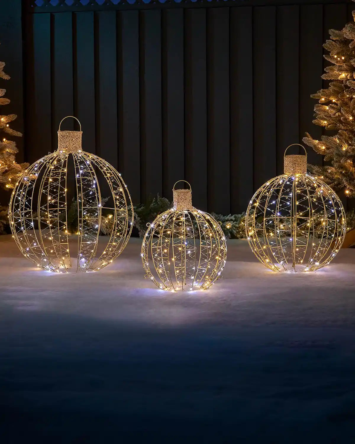 Set of three pre-lit gold bauble silhouettes displayed outdoors with warm and bright white lights.