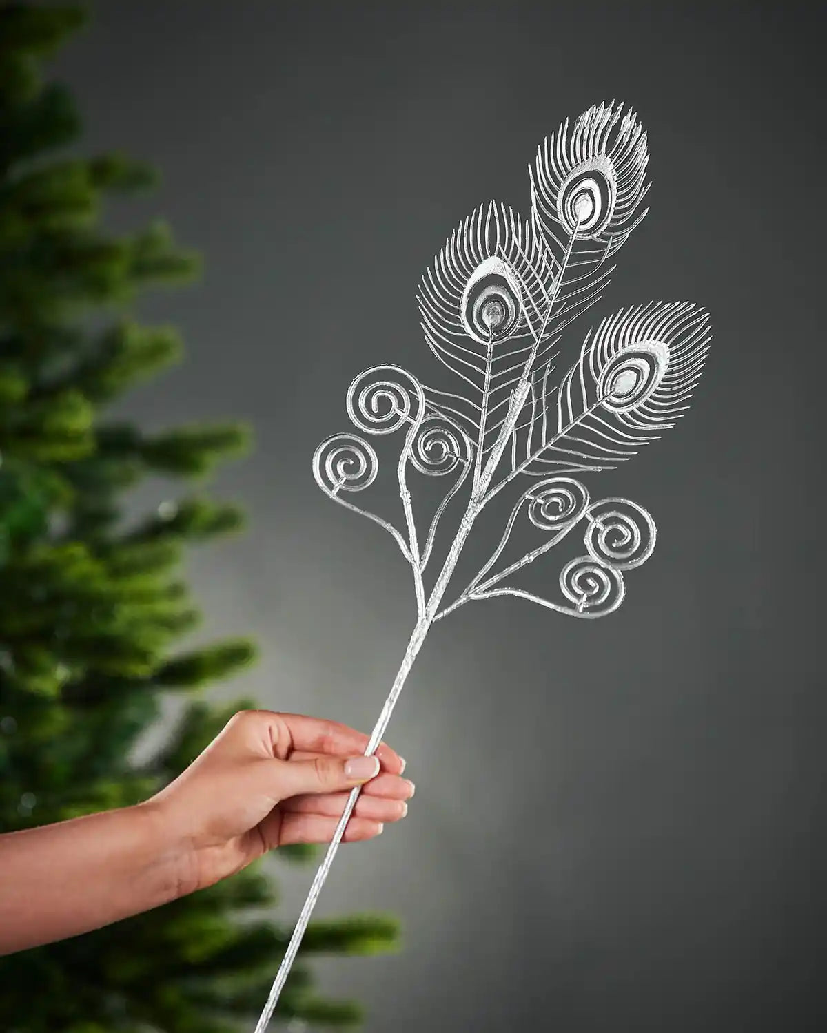 62 cm silver artificial feather pick held beside a Christmas tree