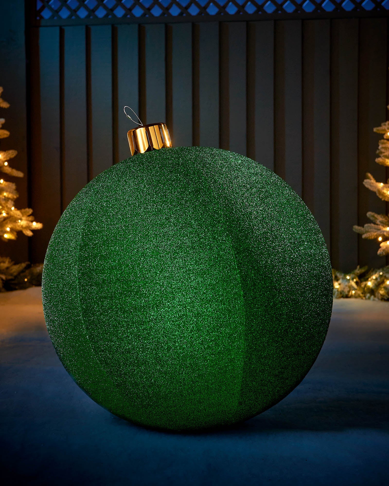 Large green 66cm inflatable tinsel Christmas bauble with a gold cap in an outdoor festive display.