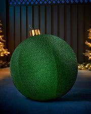 Large green 66cm inflatable tinsel Christmas bauble with a gold cap in an outdoor festive display.