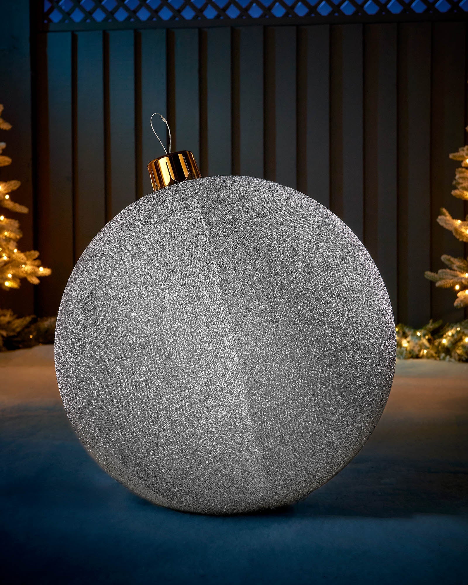 Large silver 66cm inflatable tinsel Christmas bauble with a gold cap in an outdoor festive display.