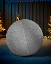 Large silver 66cm inflatable tinsel Christmas bauble with a gold cap in an outdoor festive display.