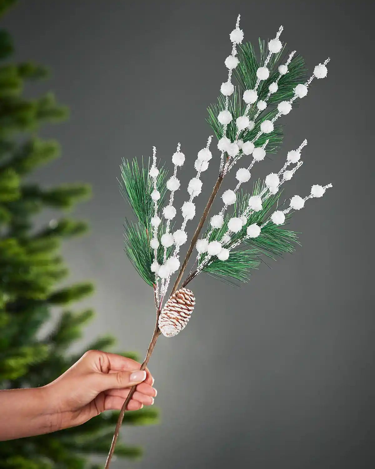 66 cm white artificial berries and pine cone pick held beside a Christmas tree