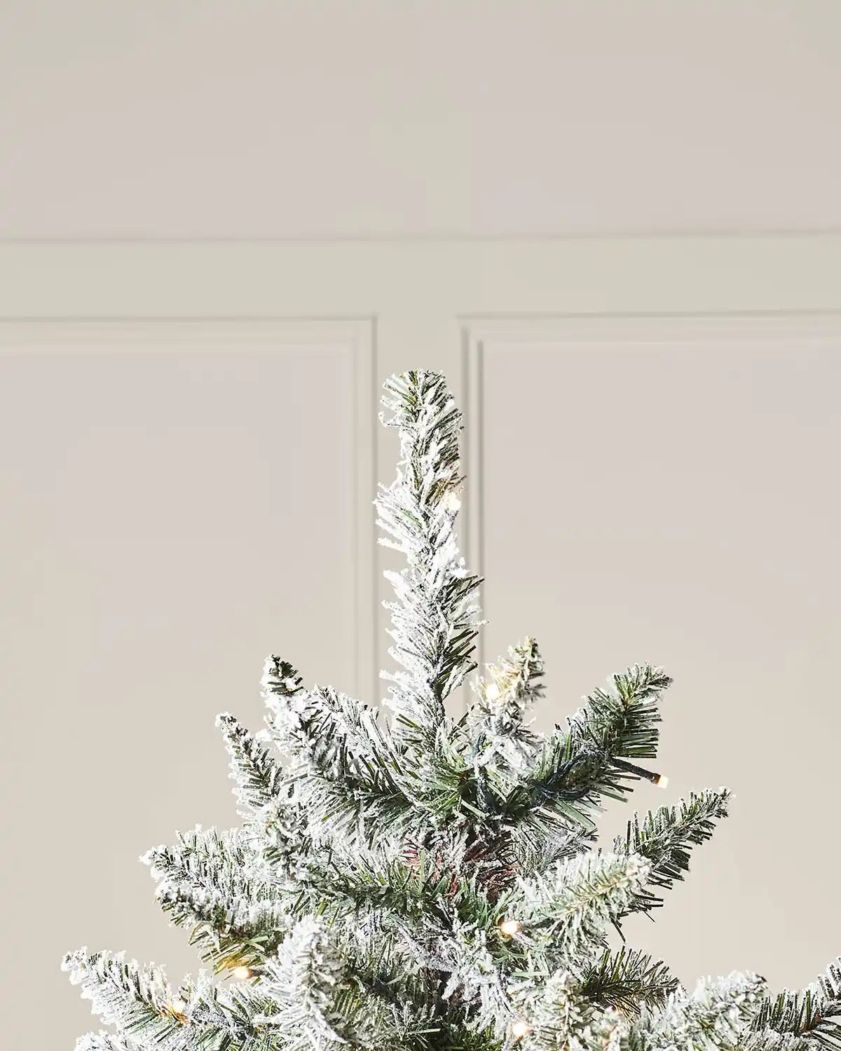 Close-up of the top section of a 6 ft full bodied snow flocked Christmas tree with pre-lit snowy branches