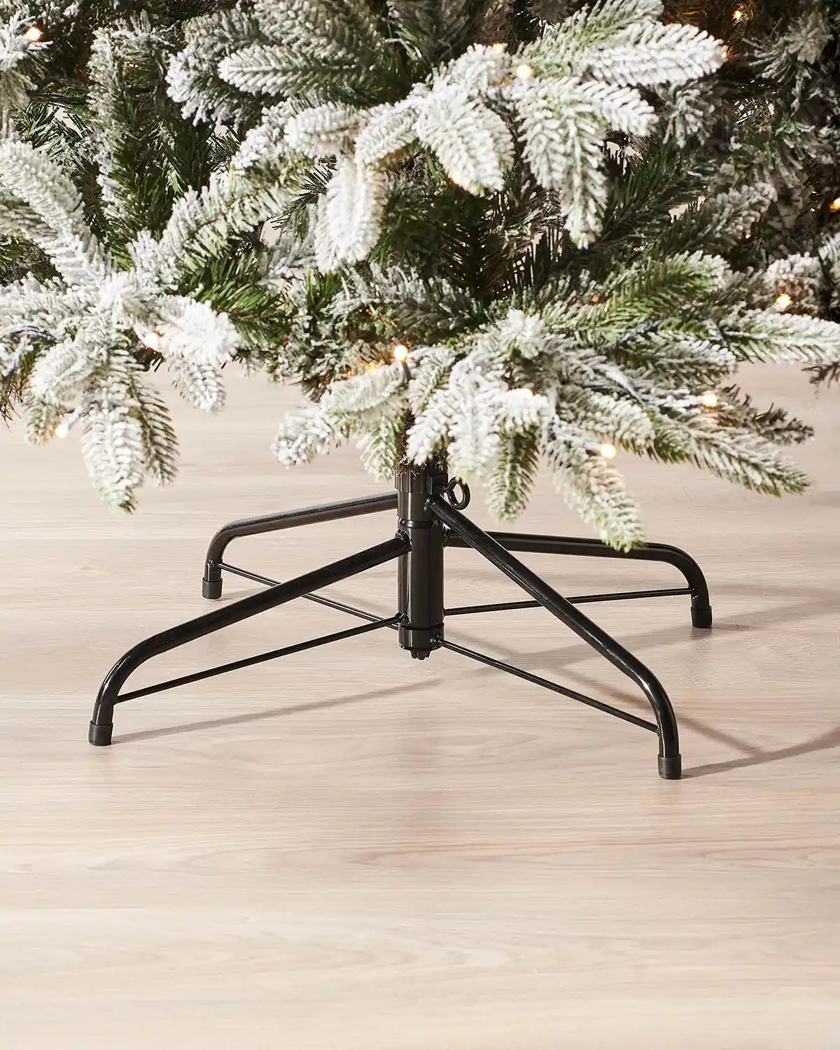 Close-up of the black metal stand and lower snow flocked branches of a 6 ft pre-lit slim Christmas tree