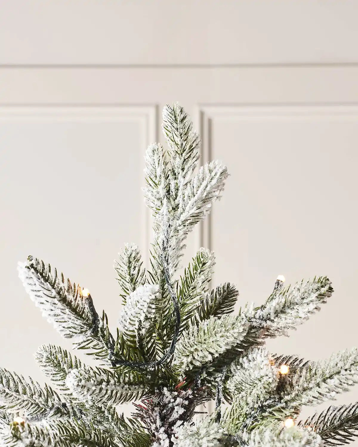 Close-up of the top section of a 6 ft slim snow flocked Christmas tree with pre-lit snowy branches