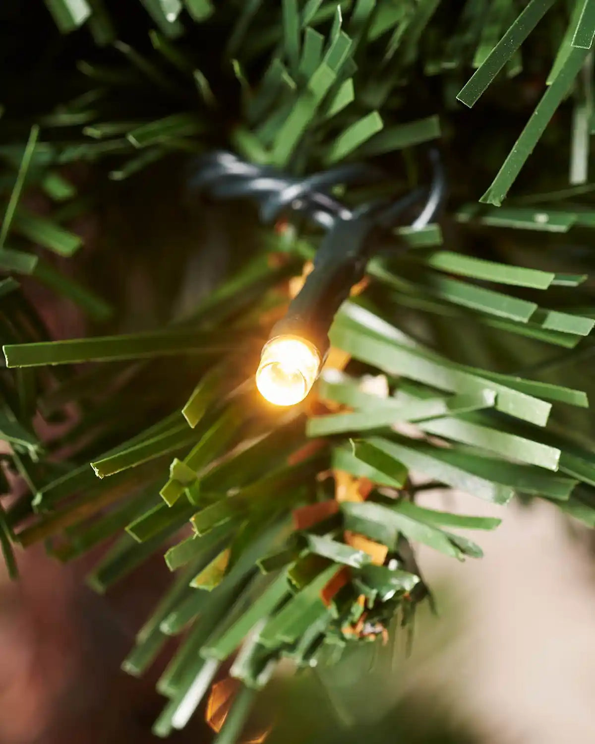 Close-up of a warm white LED light among green Christmas tree branches