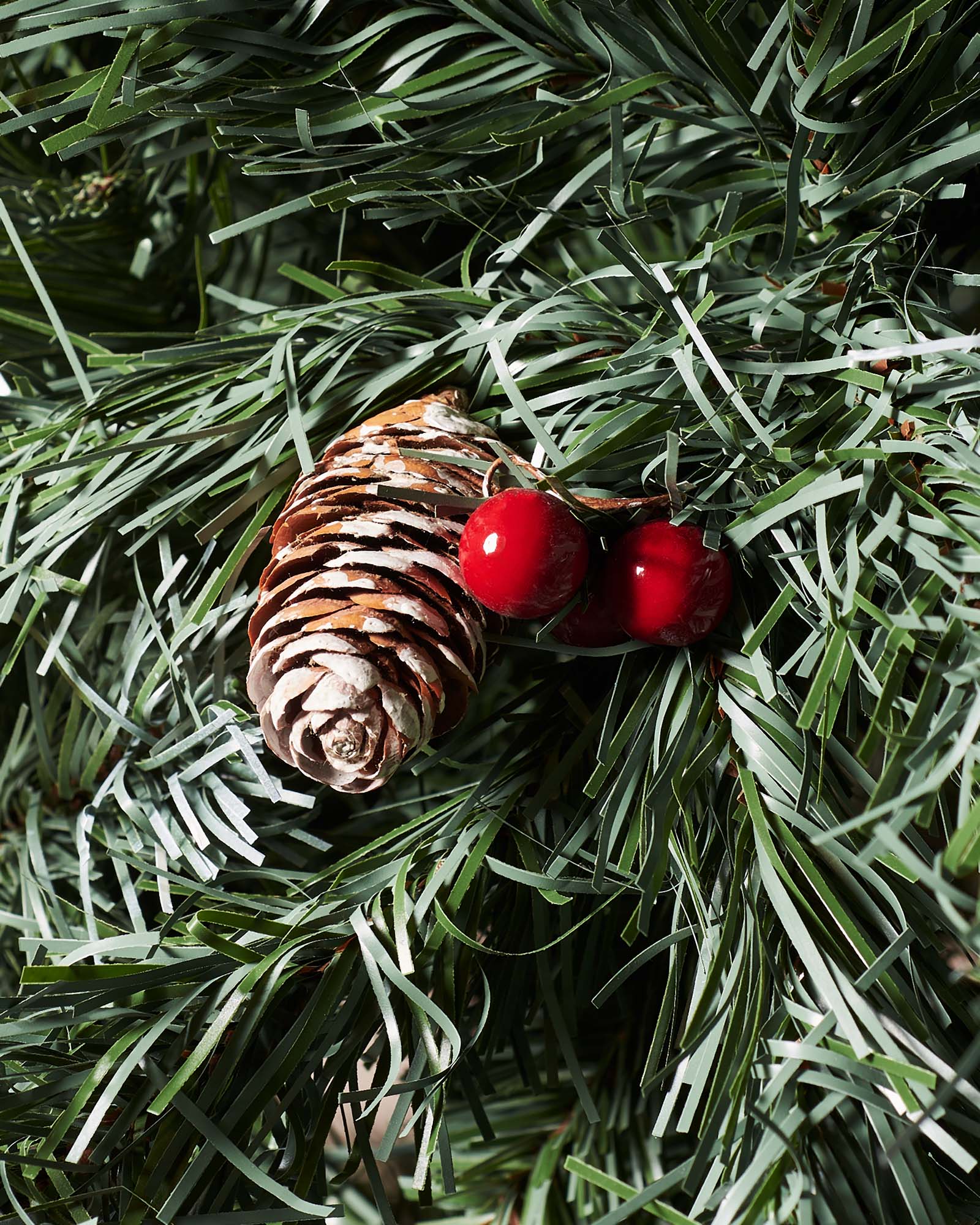 Close-up of a frosted pinecone and red berries on a Scandinavian blue spruce Christmas tree