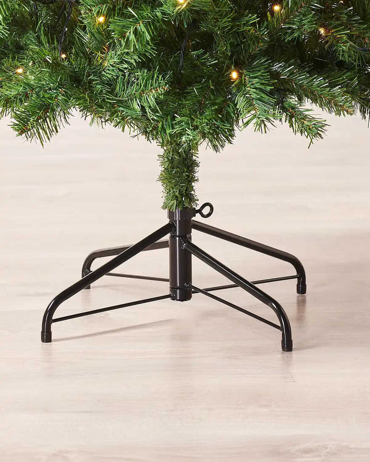 Base detail of 6ft slim Christmas tree showing lower green branches, warm white lights and metal tree stand