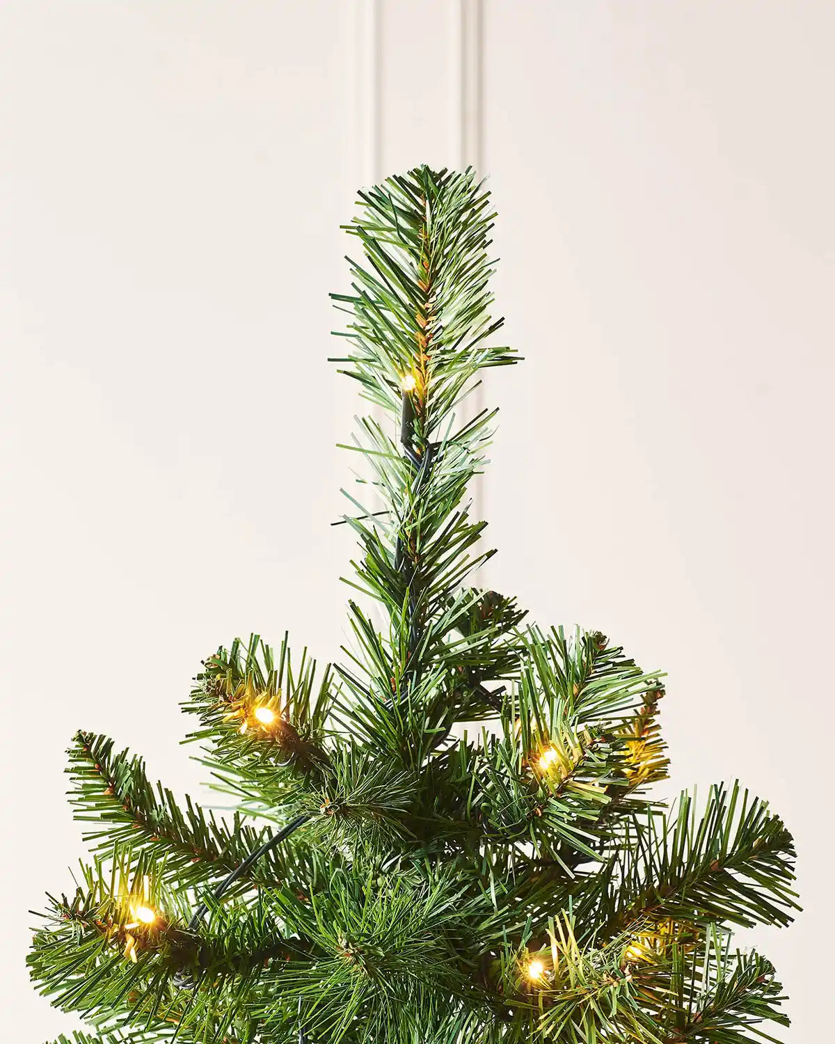 Top branch detail of 6ft slim Christmas tree with green foliage and warm white LEDs