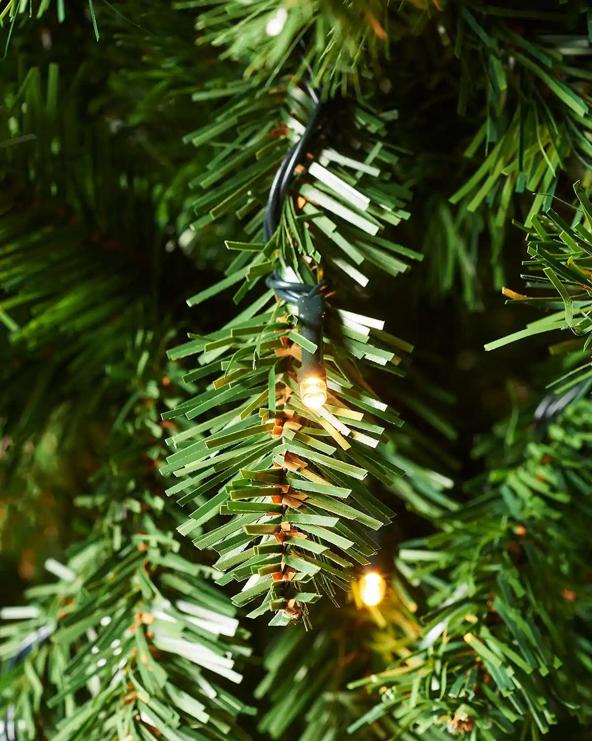 Detailed close-up of green Christmas tree foliage with a warm white LED light