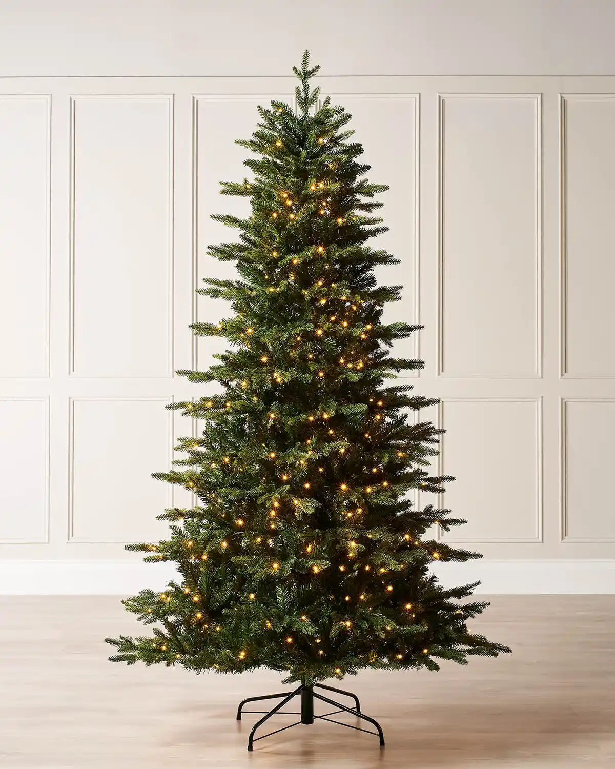 6ft Himalayan Fir Christmas Tree with lights and Black tree stand on a cream panel textured wallpaper
