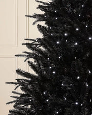 Close-up of 6ft pre-lit black pine tree branches in front of white panelling background