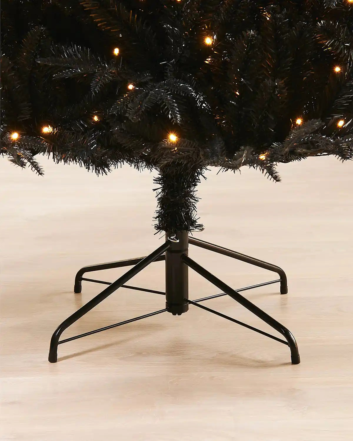 Close-up of 6ft pre-lit black pine Christmas tree black stand on light wood flooring