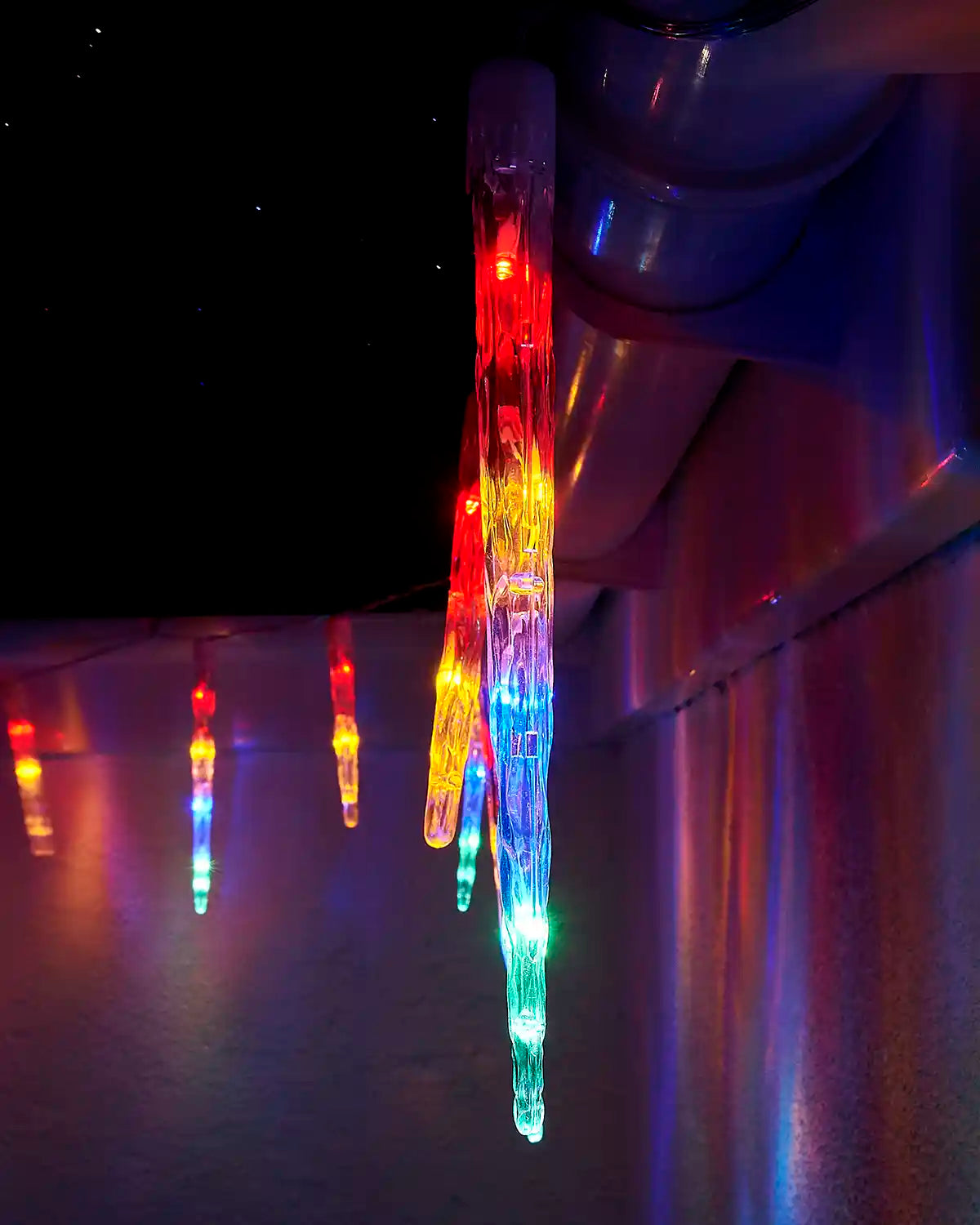 Close-up of a multi-colour LED icicle drop light hanging from a roofline.
