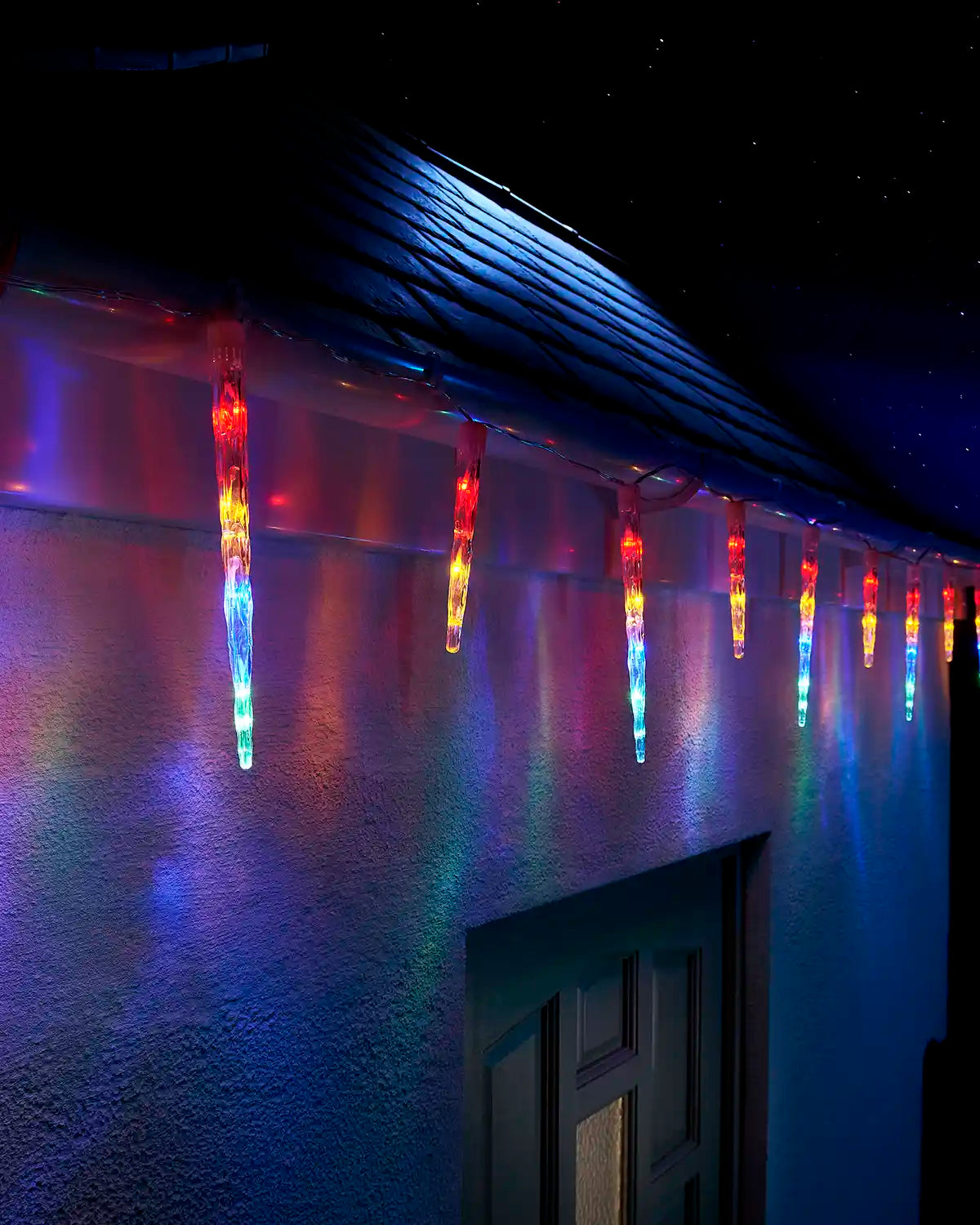 Multi-colour icicle drop lights displayed along a house roofline at night.