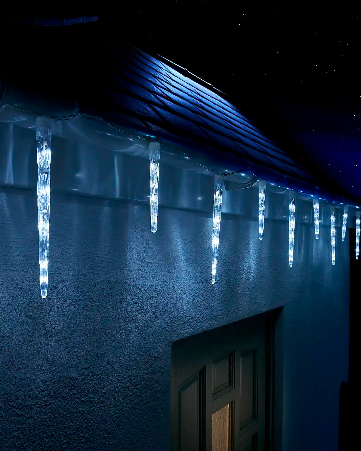 White icicle drop lights displayed along a house roofline at night.