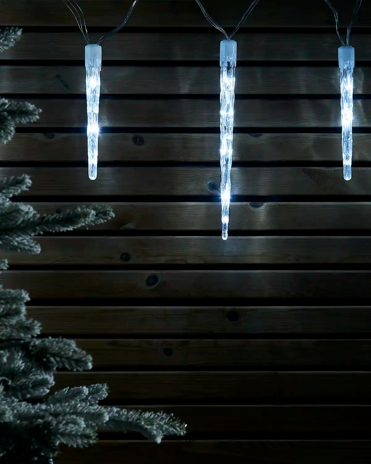 White icicle drop lights displayed against a dark wooden wall.