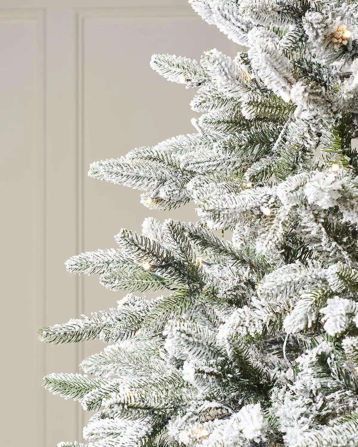 Close-up of snow flocked Christmas tree branches with realistic green foliage and warm white LEDs