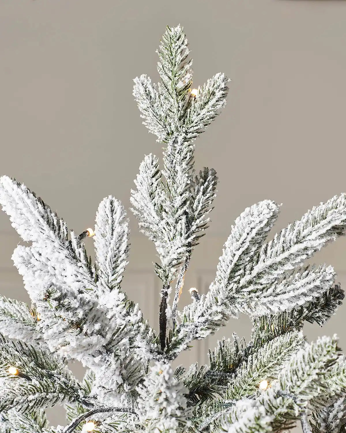Close-up of the top section of a 7.5 ft snow flocked Christmas tree with pre-lit branches