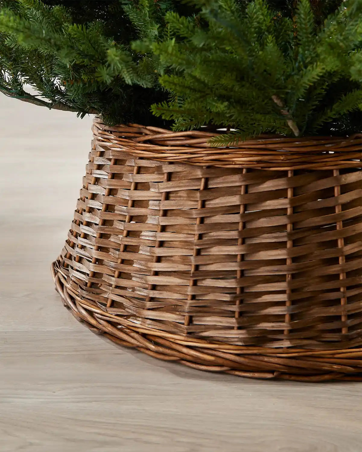 Close-up of the 70cm brown wicker tree collar showing the woven rattan texture beneath green Christmas tree branches.