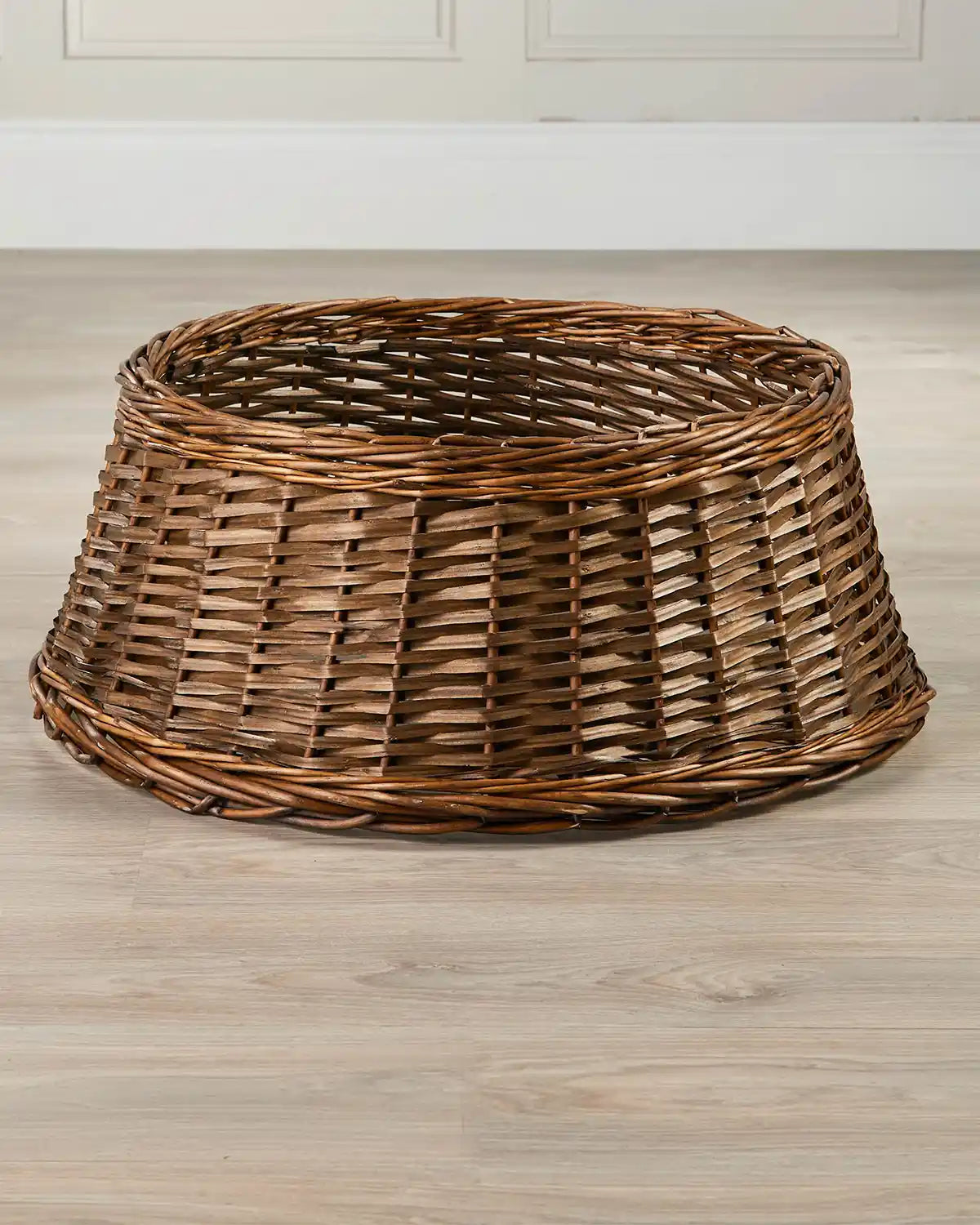 70cm brown wicker tree collar displayed indoors on a wooden floor, showing its tapered shape and open top.