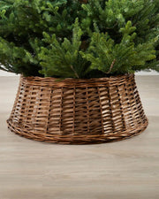 70cm brown wicker tree collar placed around the base of a Christmas tree on an indoor wooden floor.