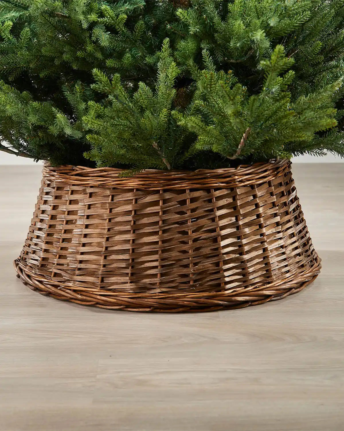 70cm brown wicker tree collar placed around the base of a Christmas tree on an indoor wooden floor.