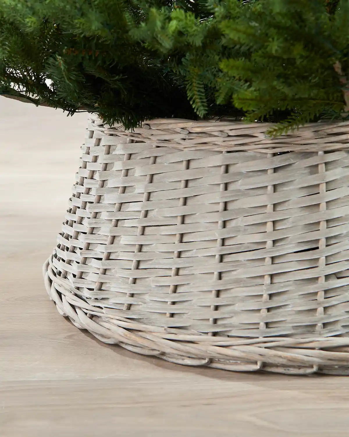 Close-up of the 70cm grey wicker tree collar showing the woven rattan texture beneath green Christmas tree branches.