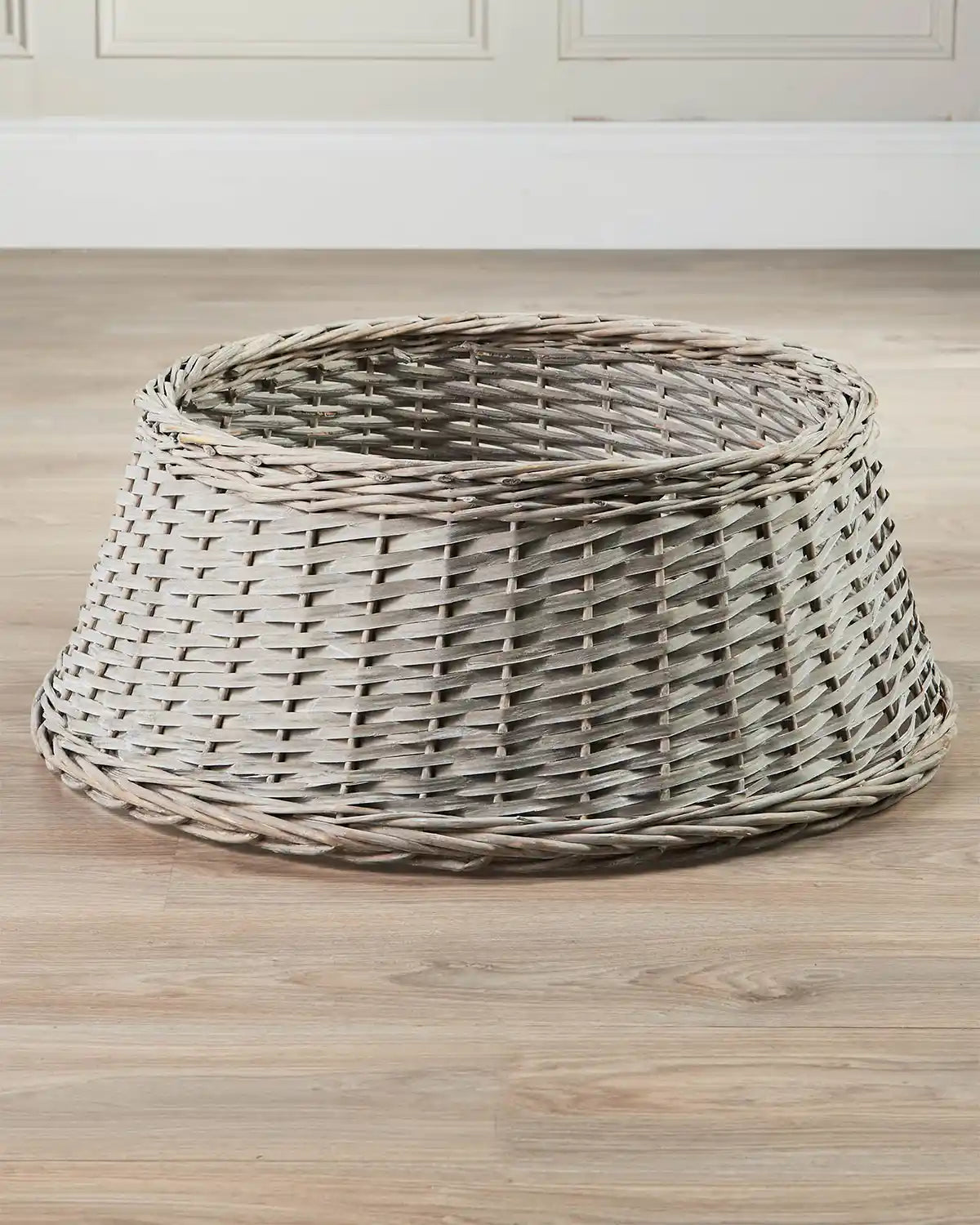 70cm grey wicker tree collar displayed indoors on a wooden floor, showing its tapered shape and open top.
